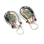 A pair of Prehnite smooth oval earrings with cool inclusions, adorned with hammered bronze, twisted oxidized sterling silver, and micro faceted watermelon tourmaline gemstones, attached to sterling silver French hooks.