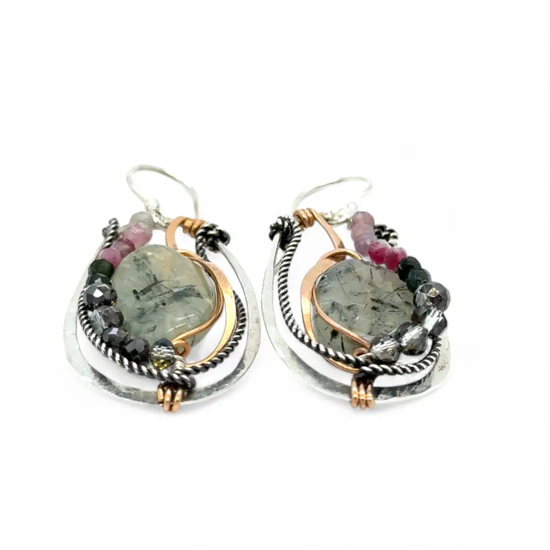 A pair of Prehnite smooth oval earrings with cool inclusions, adorned with hammered bronze, twisted oxidized sterling silver, and micro faceted watermelon tourmaline gemstones, attached to sterling silver French hooks.