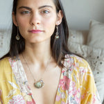 A Prehnite faceted coin gemstone with a mauve faceted moonstone set in bronze hammered wire inside a textured darkened sterling pendant, accented with green cat's eye faceted gemstones and a crystal finish.