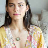 A Prehnite faceted coin gemstone with a mauve faceted moonstone set in bronze hammered wire inside a textured darkened sterling pendant, accented with green cat's eye faceted gemstones and a crystal finish.