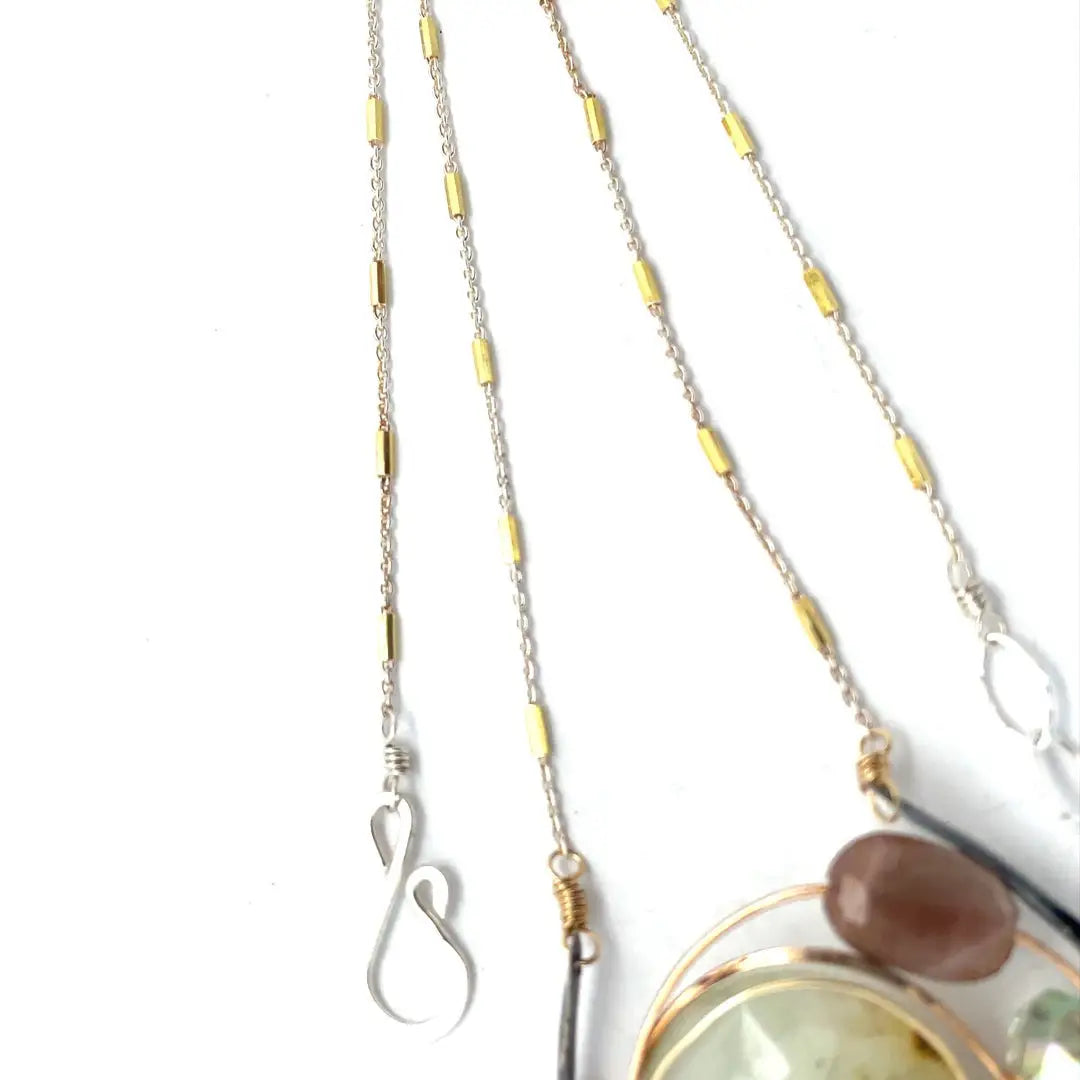 A Prehnite faceted coin gemstone with a mauve faceted moonstone set in bronze hammered wire inside a textured darkened sterling pendant, accented with green cat's eye faceted gemstones and a crystal finish.