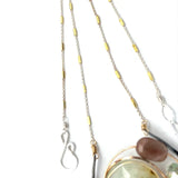 A Prehnite faceted coin gemstone with a mauve faceted moonstone set in bronze hammered wire inside a textured darkened sterling pendant, accented with green cat's eye faceted gemstones and a crystal finish.