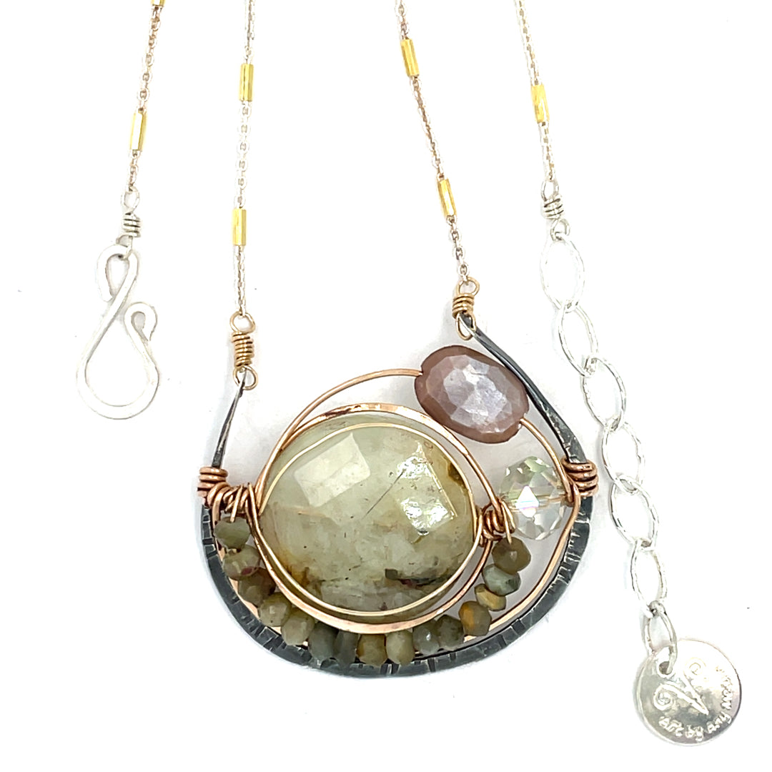 A Prehnite faceted coin gemstone with a mauve faceted moonstone set in bronze hammered wire inside a textured darkened sterling pendant, accented with green cat's eye faceted gemstones and a crystal finish.