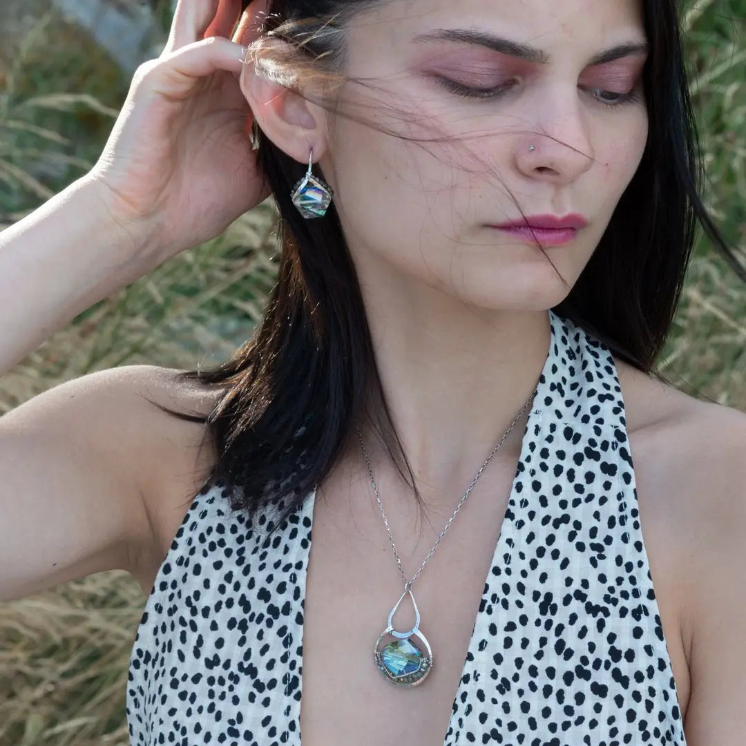 A sterling silver necklace with a box chain and an oval citrus crystal pendant, surrounded by smaller faceted crystals on dark haired woman.