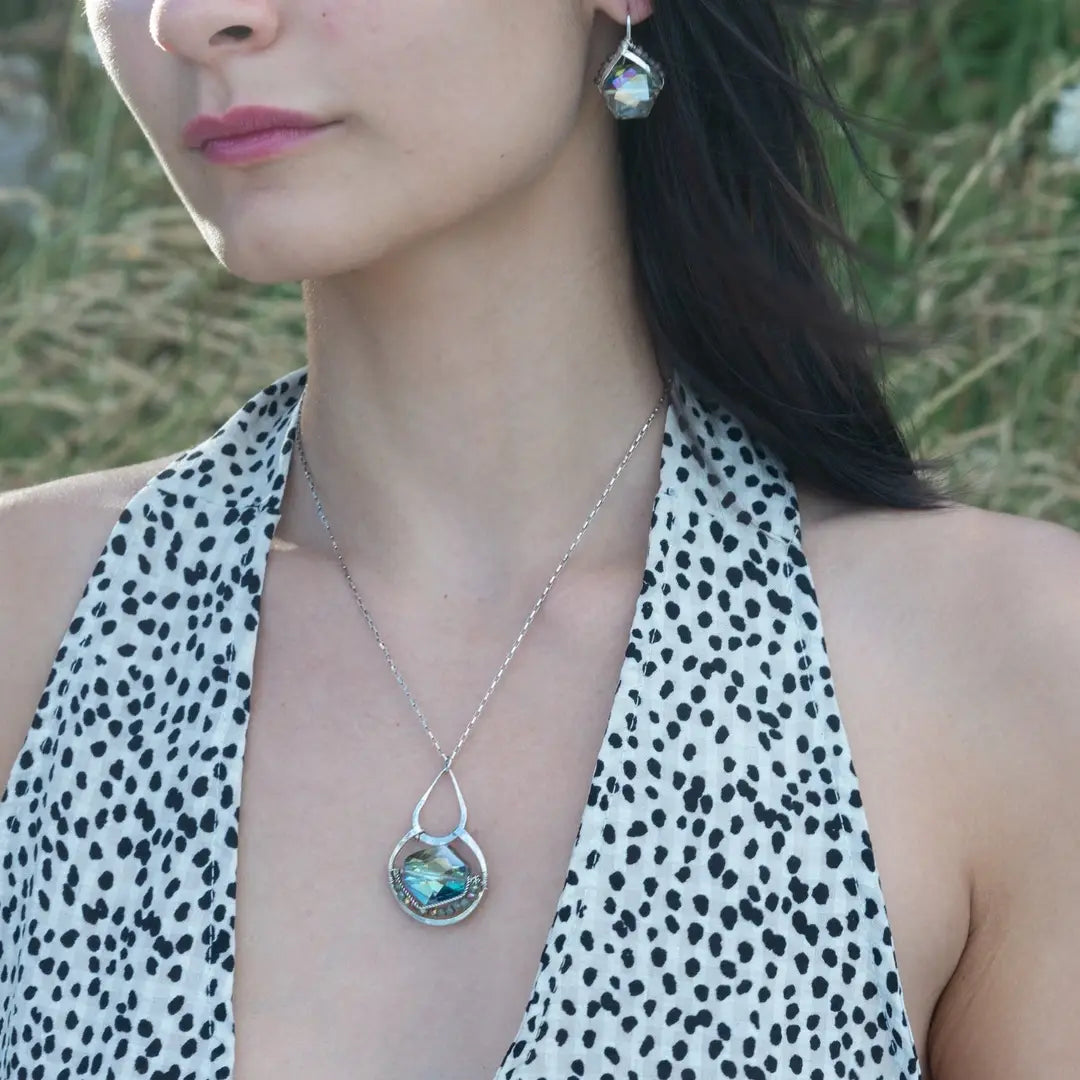 A sterling silver necklace with a box chain and an oval citrus crystal pendant, surrounded by smaller faceted crystals on a dark haired woman.