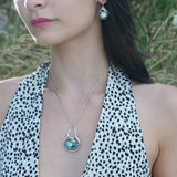 A sterling silver necklace with a box chain and an oval citrus crystal pendant, surrounded by smaller faceted crystals on a dark haired woman.