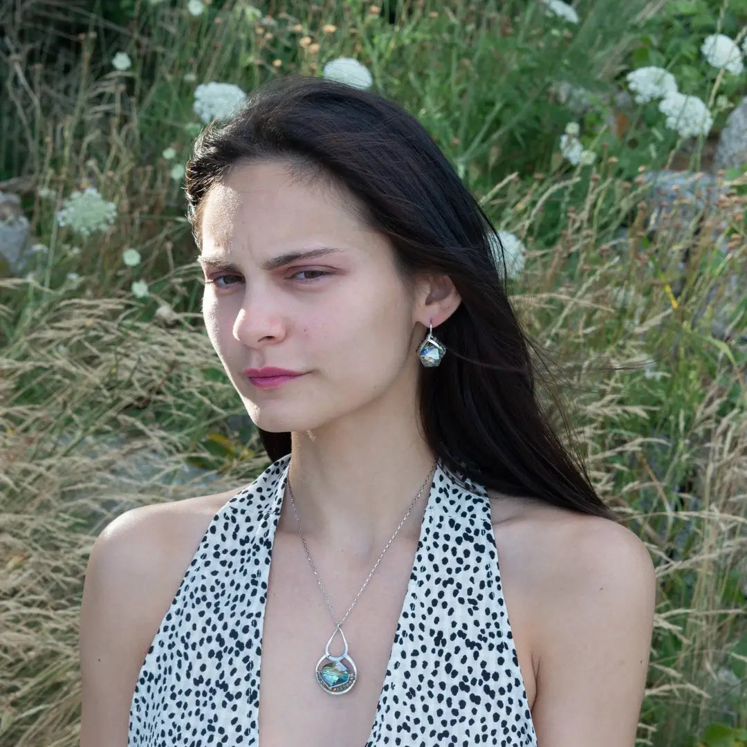 A sterling silver necklace with a box chain and an oval citrus crystal pendant, surrounded by smaller faceted crystals on a dark haired woman.