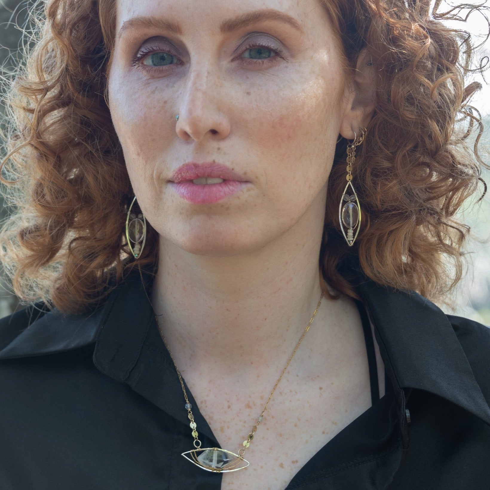 A person wearing sterling silver earrings with quartz and opal gemstones, suspended from gold filled coin chain.