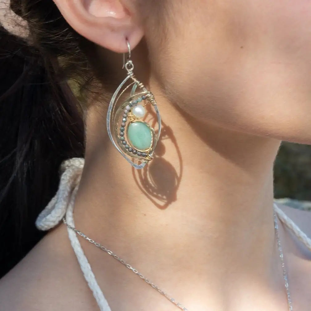 A pair of sterling silver marquise earrings with blue tourmaline gemstones, fresh water pearl, and jade set in hammered brass with silver french hooks.