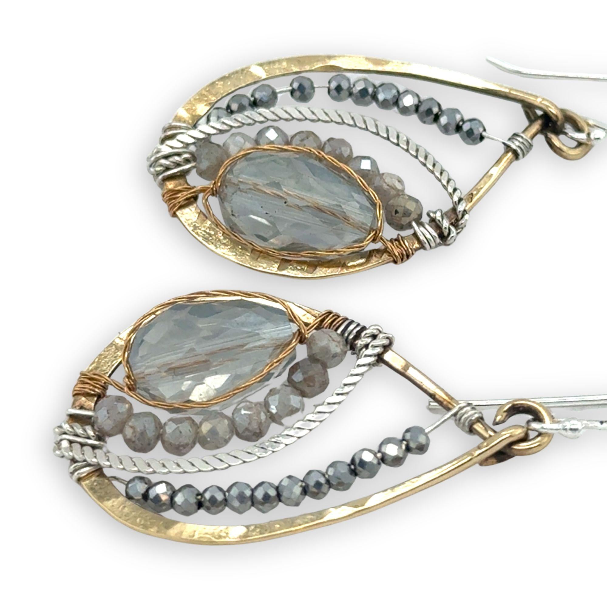 a light blue crystal drop wrapped in brass twist wire is surrounded by moonstone, pyrite gemstones, and hammered sterling silver hammered twist inside a mini brass teardrop earring