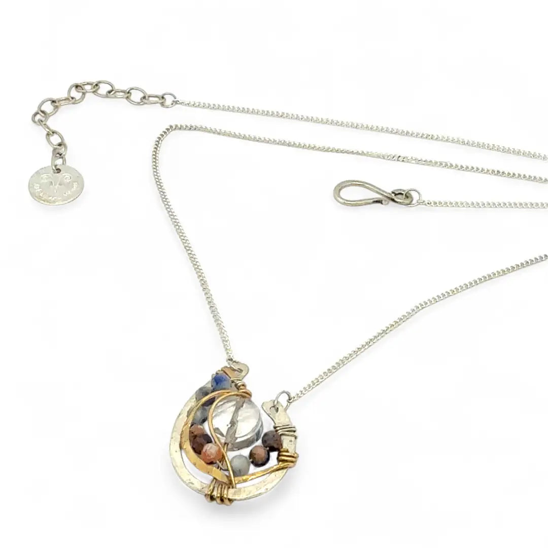 quartz coin surrounded by layers of hammered brass wire and sodalite gemstones within a mini sterling silver pendant necklace