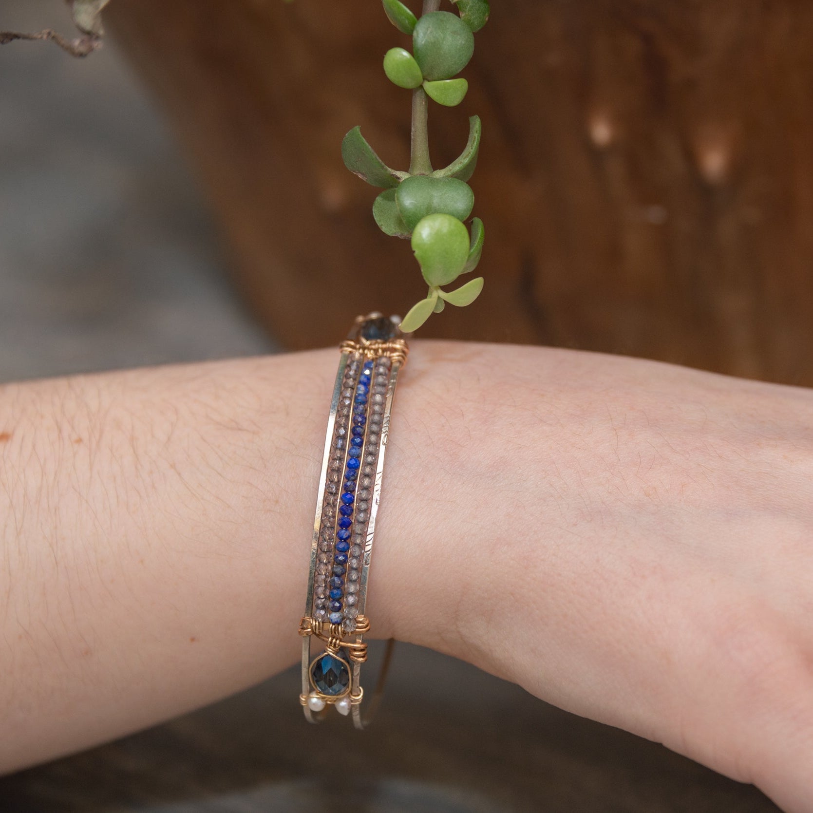 A slim handmade hammered sterling silver bracelet with bronze bars attached by lapis and blue quartz gemstones, on each side is accented with blue crystal drops and fresh water pearls