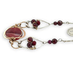 Red striped agate wrapped in hammered bronze wire suspended between sterling silver hammered petals holding faceted garnet and red crystal gemstones on a sterling silver bar chain necklace