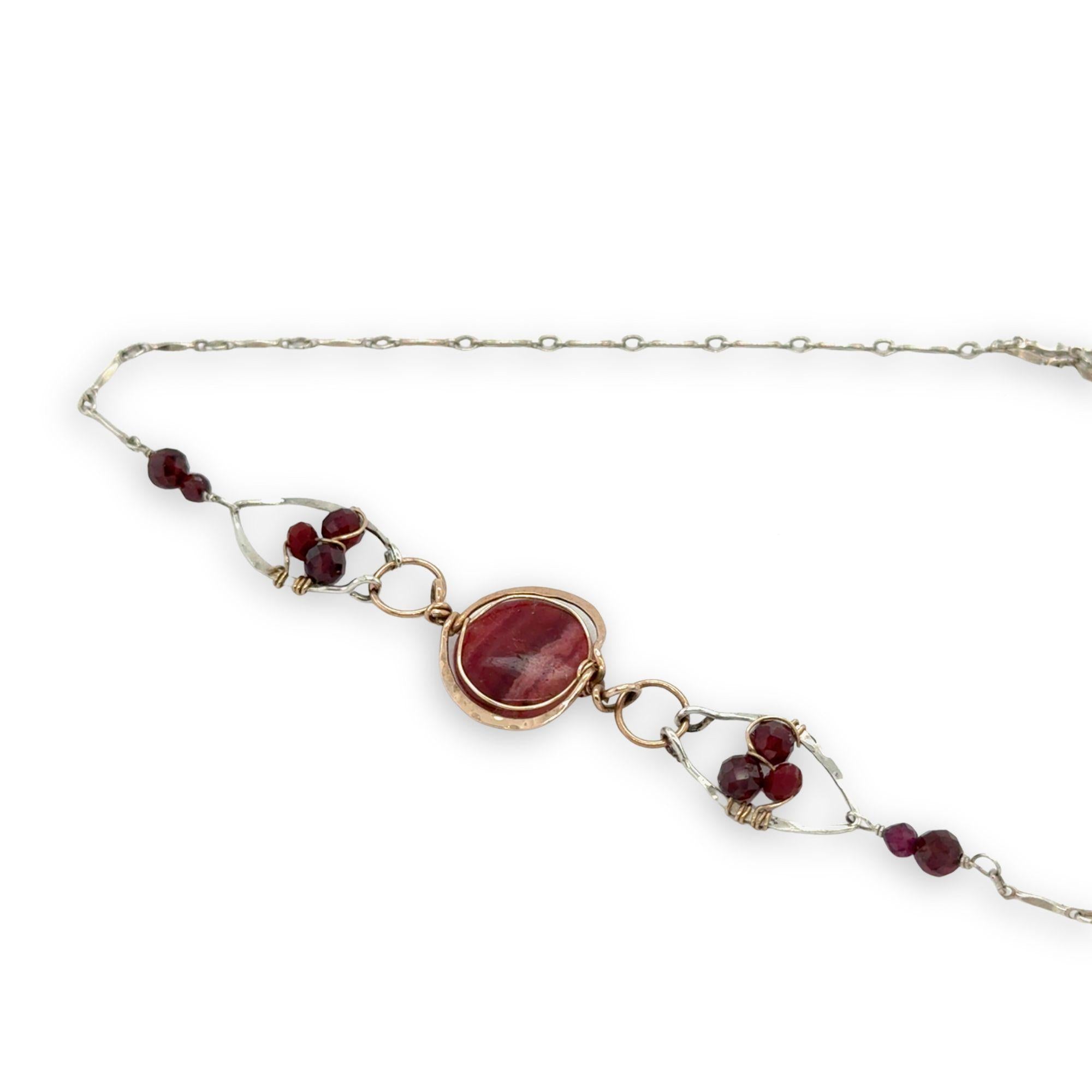 Red striped agate wrapped in hammered bronze wire suspended between sterling silver hammered petals holding faceted garnet and red crystal gemstones on a sterling silver bar chain necklace