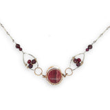 Red striped agate wrapped in hammered bronze wire suspended between sterling silver hammered petals holding faceted garnet and red crystal gemstones on a sterling silver bar chain necklace