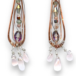 Rose quartz smooth drops dangle from a copper skinny drop earring holding pink crystal, green amethyst, rutilated cherry quartz, and sterling silver wire