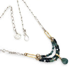 A necklace with blue tourmaline faceted ombre gemstones and silver crystal cubes, featuring a moss agate drop, hammered brass rectangle links, and a handmade hammered brass strap on sterling silver chain