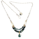 A necklace with blue tourmaline faceted ombre gemstones and silver crystal cubes, featuring a moss agate drop, hammered brass rectangle links, and a handmade hammered brass strap on sterling silver chain