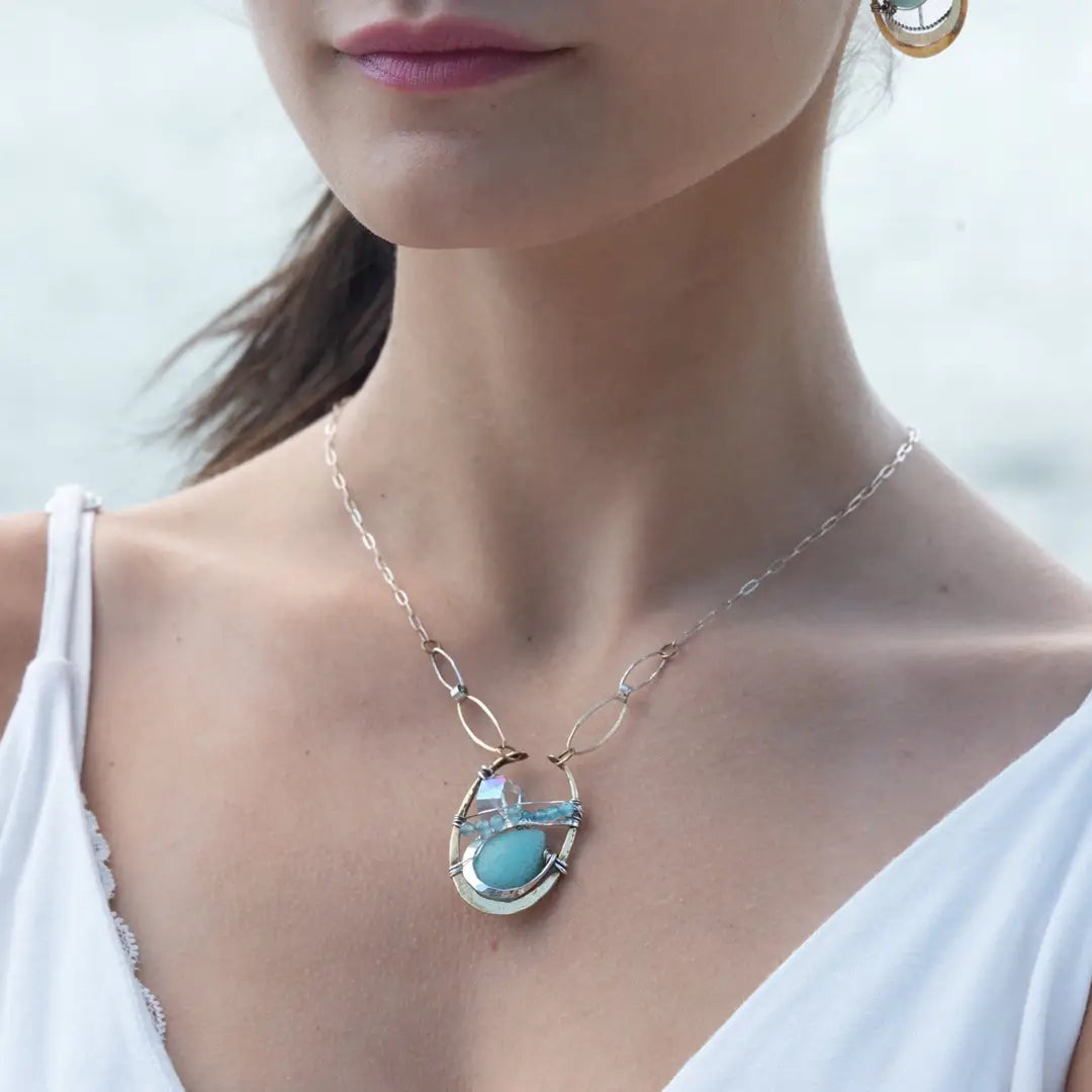 A sterling silver brass oval pendant necklace with a blue amazonite smooth gemstone drop and accents of micro faceted cats eye gems, atmospheric crystals, and gold-filled links on a delicate chain.