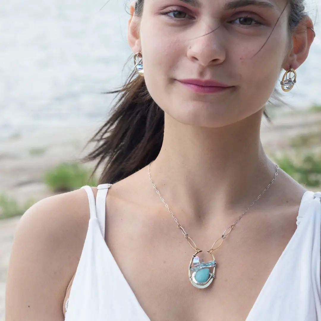 A sterling silver brass oval pendant necklace with a blue amazonite smooth gemstone drop and accents of micro faceted cats eye gems, atmospheric crystals, and gold-filled links on a delicate chain.