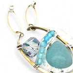 A sterling silver brass oval pendant necklace with a blue amazonite smooth gemstone drop and accents of micro faceted cats eye gems, atmospheric crystals, and gold-filled links on a delicate chain.