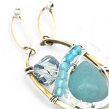 A sterling silver brass oval pendant necklace with a blue amazonite smooth gemstone drop and accents of micro faceted cats eye gems, atmospheric crystals, and gold-filled links on a delicate chain.
