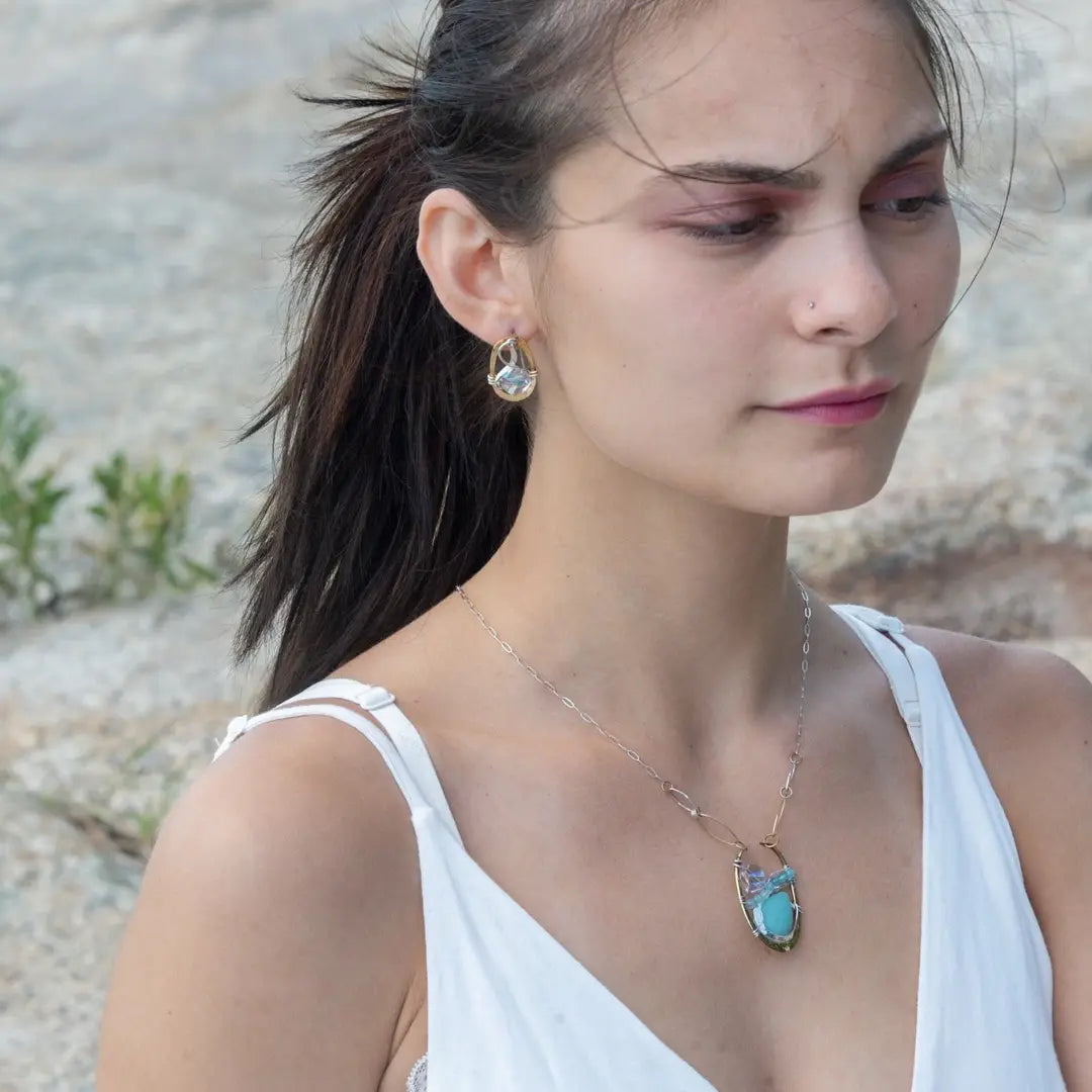 A sterling silver brass oval pendant necklace with a blue amazonite smooth gemstone drop and accents of micro faceted cats eye gems, atmospheric crystals, and gold-filled links on a delicate chain.