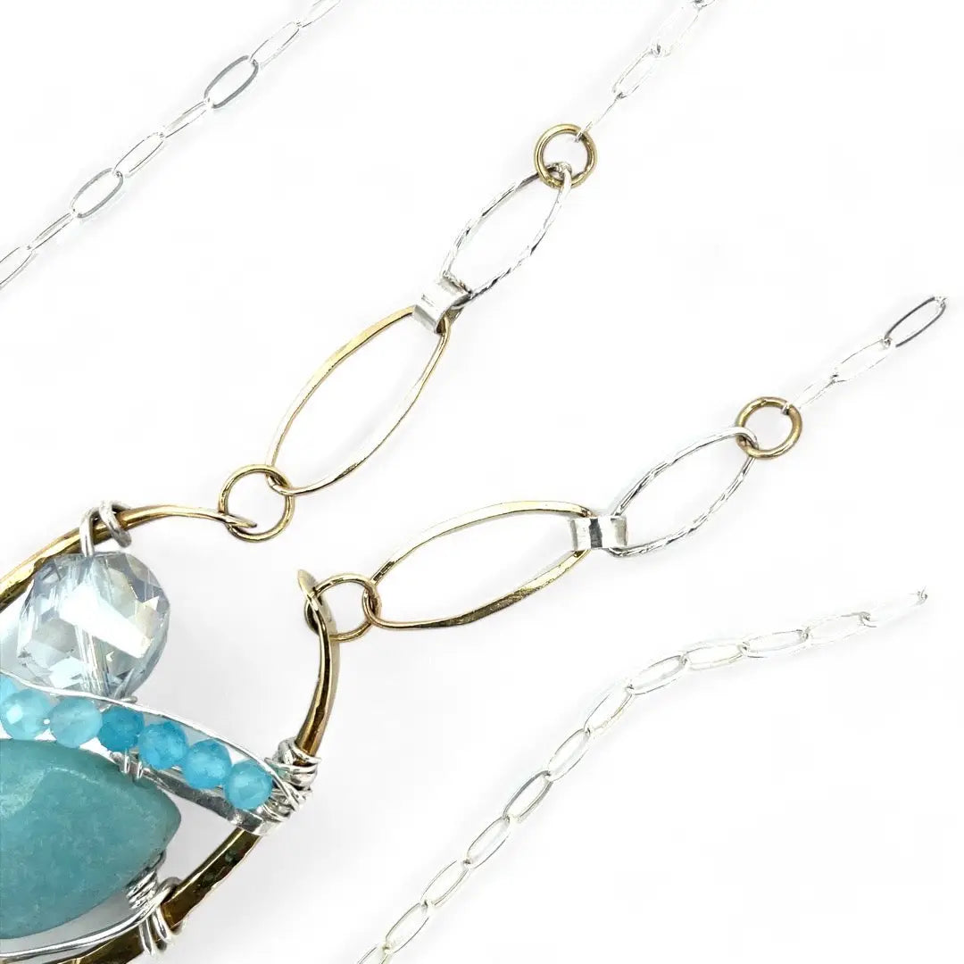 A sterling silver brass oval pendant necklace with a blue amazonite smooth gemstone drop and accents of micro faceted cats eye gems, atmospheric crystals, and gold-filled links on a delicate chain.