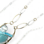 A sterling silver brass oval pendant necklace with a blue amazonite smooth gemstone drop and accents of micro faceted cats eye gems, atmospheric crystals, and gold-filled links on a delicate chain.