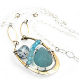 A sterling silver brass oval pendant necklace with a blue amazonite smooth gemstone drop and accents of micro faceted cats eye gems, atmospheric crystals, and gold-filled links on a delicate chain.
