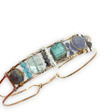 Flashy labradorite, aquamarine, iolite, and apatite gemstones wrapped tightly in sterling silver and brass twist wires are attached to a hammered bronze cuff bracelet