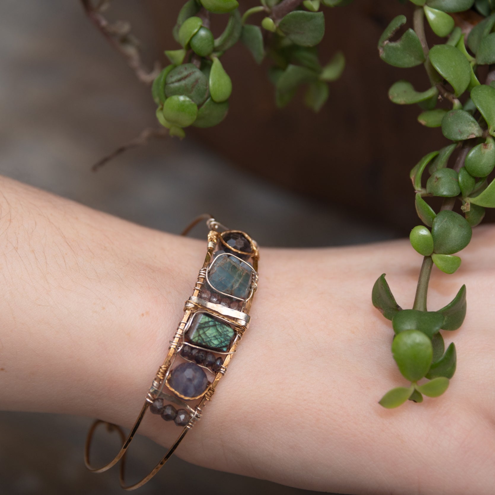 Flashy labradorite, aquamarine, iolite, and apatite gemstones wrapped tightly in sterling silver and brass twist wires are attached to a hammered bronze cuff bracelet