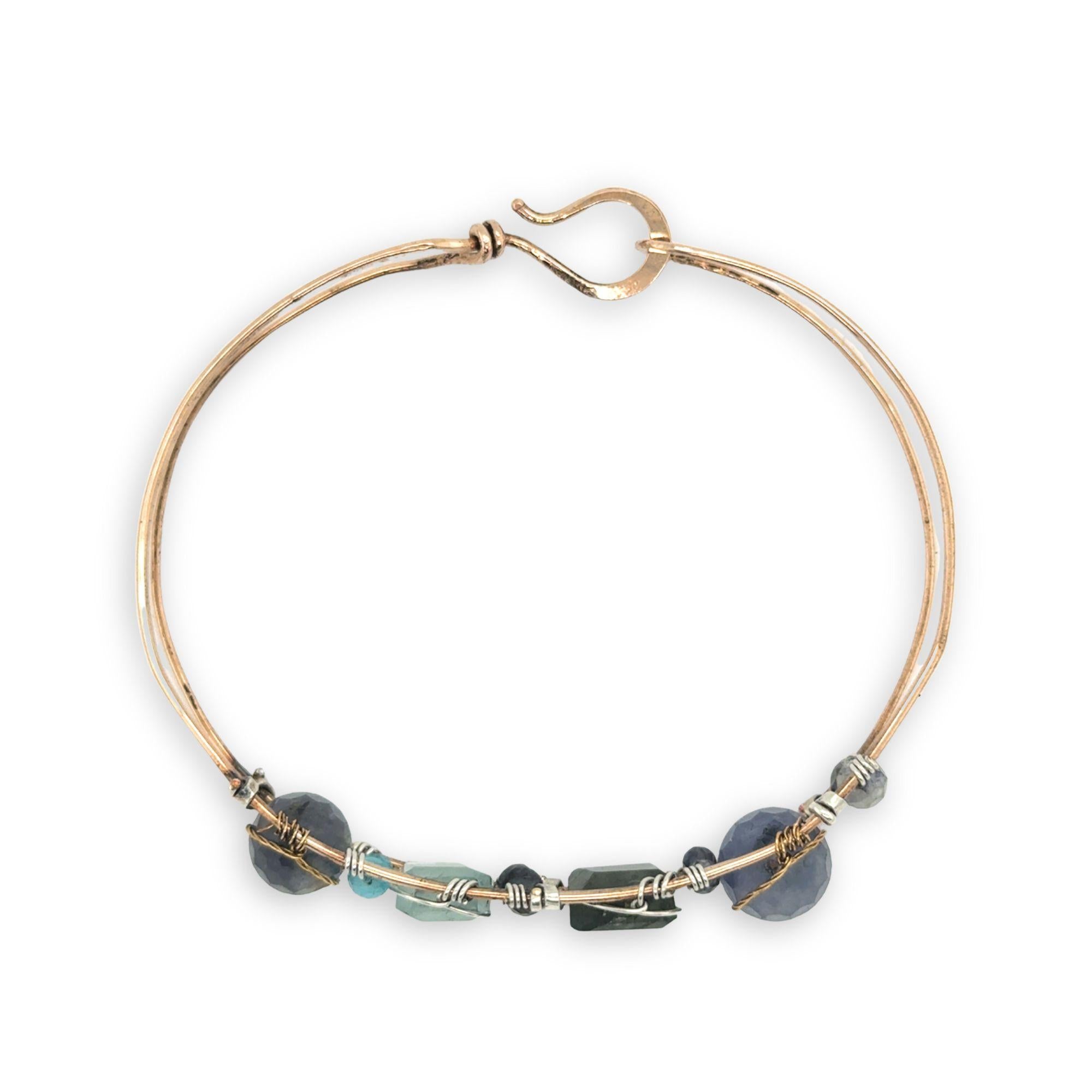 Flashy labradorite, aquamarine, iolite, and apatite gemstones wrapped tightly in sterling silver and brass twist wires are attached to a hammered bronze cuff bracelet