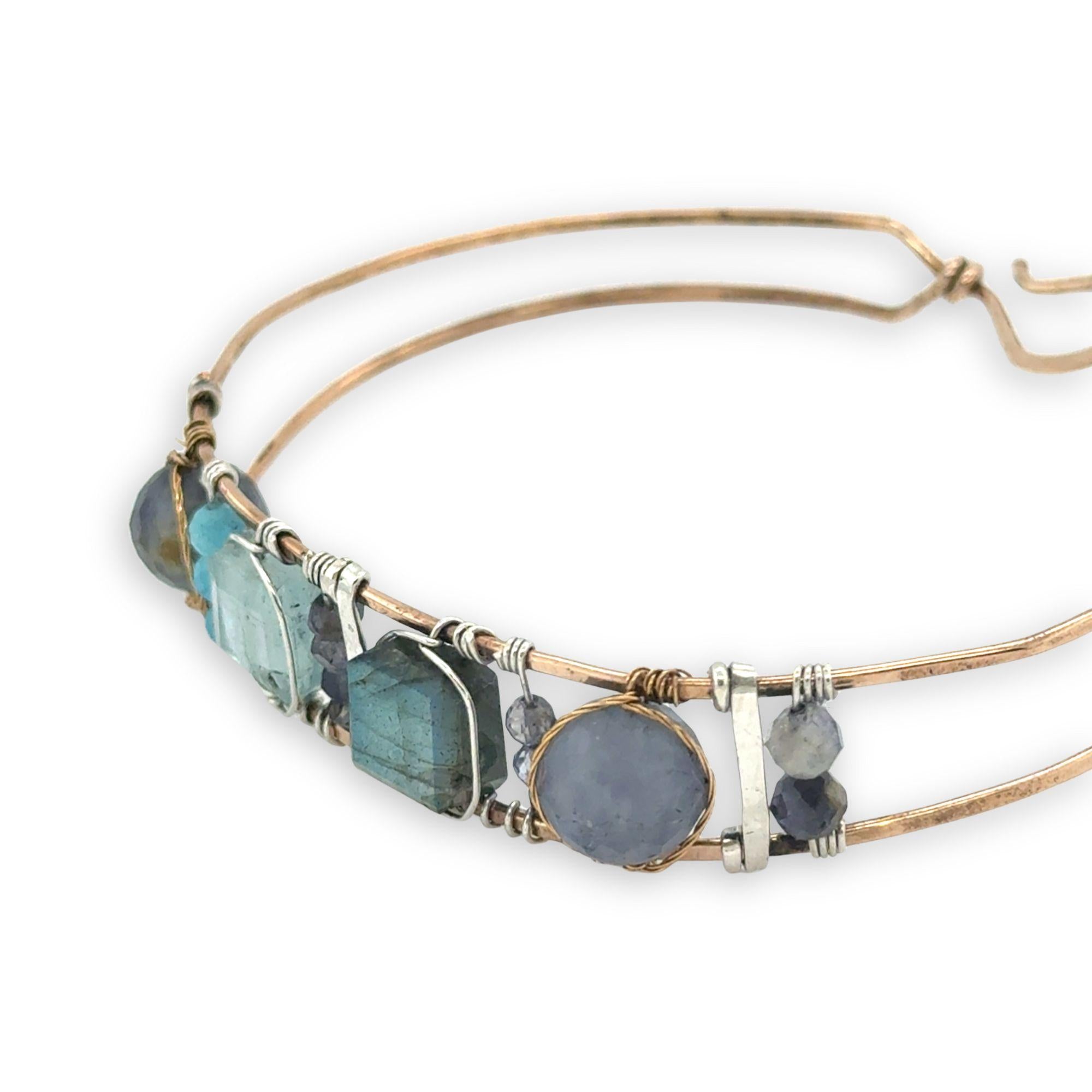 Flashy labradorite, aquamarine, iolite, and apatite gemstones wrapped tightly in sterling silver and brass twist wires are attached to a hammered bronze cuff bracelet