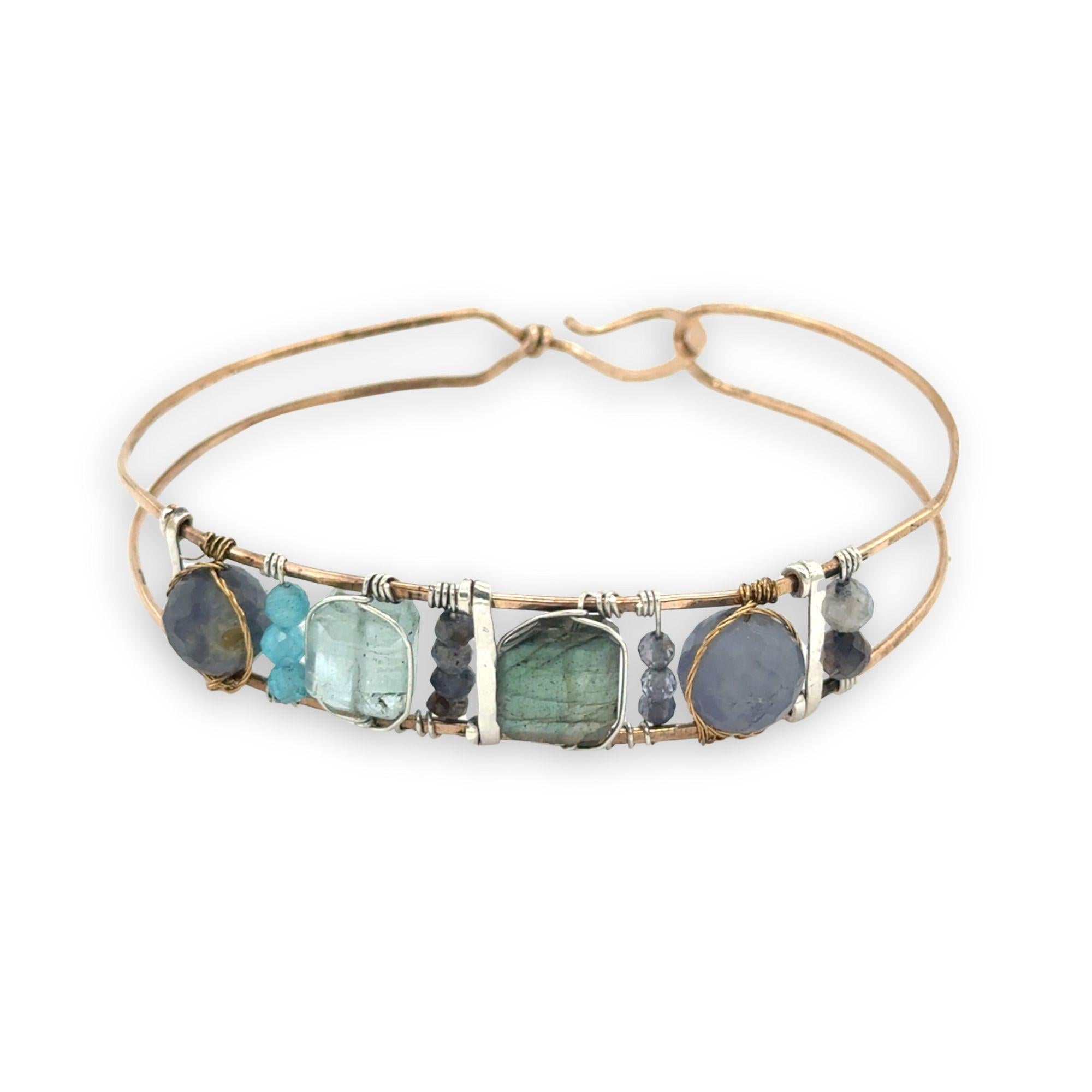 Flashy labradorite, aquamarine, iolite, and apatite gemstones wrapped tightly in sterling silver and brass twist wires are attached to a hammered bronze cuff bracelet