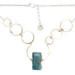 A bronze statement necklace made up of various sized rings with a blue quartz raw slab gemstone  on sterling silver delicate doubled chain