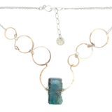 A bronze statement necklace made up of various sized rings with a blue quartz raw slab gemstone  on sterling silver delicate doubled chain