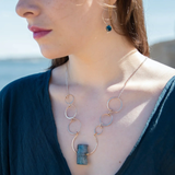 A bronze statement necklace made up of various sized rings with a blue quartz raw slab gemstone  on sterling silver delicate doubled chain