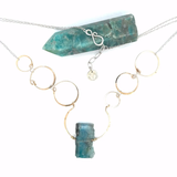 A bronze statement necklace made up of various sized rings with a blue quartz raw slab gemstone  on sterling silver delicate doubled chain