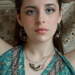 A person wearing a necklace with a hammered brass crescent pendant and double strands of sterling silver chains with Faceted cat's eye and black spinel gemstones and a clear quartz nugget