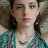 A person wearing a necklace with a hammered brass crescent pendant and double strands of sterling silver chains with Faceted cat's eye and black spinel gemstones and a clear quartz nugget