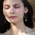 A pair of sterling silver hoop earrings with labradorite faceted coins inside mini sterling silver hammered rings, suspended from oxidized crinkle chain.