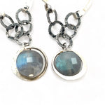 A pair of sterling silver hoop earrings with labradorite faceted coins inside mini sterling silver hammered rings, suspended from oxidized crinkle chain.