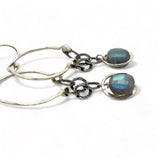 A pair of sterling silver hoop earrings with labradorite faceted coins inside mini sterling silver hammered rings, suspended from oxidized crinkle chain.