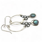 A pair of sterling silver hoop earrings with labradorite faceted coins inside mini sterling silver hammered rings, suspended from oxidized crinkle chain.