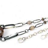 An adjustable sterling silver chain necklace with smokey quartz faceted gemstone nuggets and handmade sterling silver links with leaf patterns.