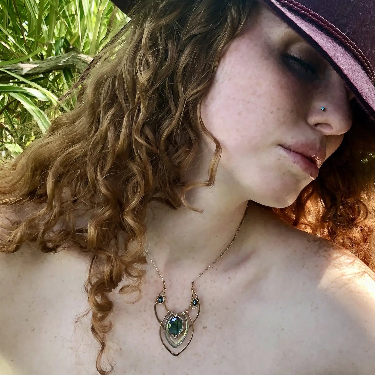 A leaf stamped silver and bronze necklace featuring a flashy labradorite gemstone with intricate metalwork and blue crystal accents on sterling silver bar chain