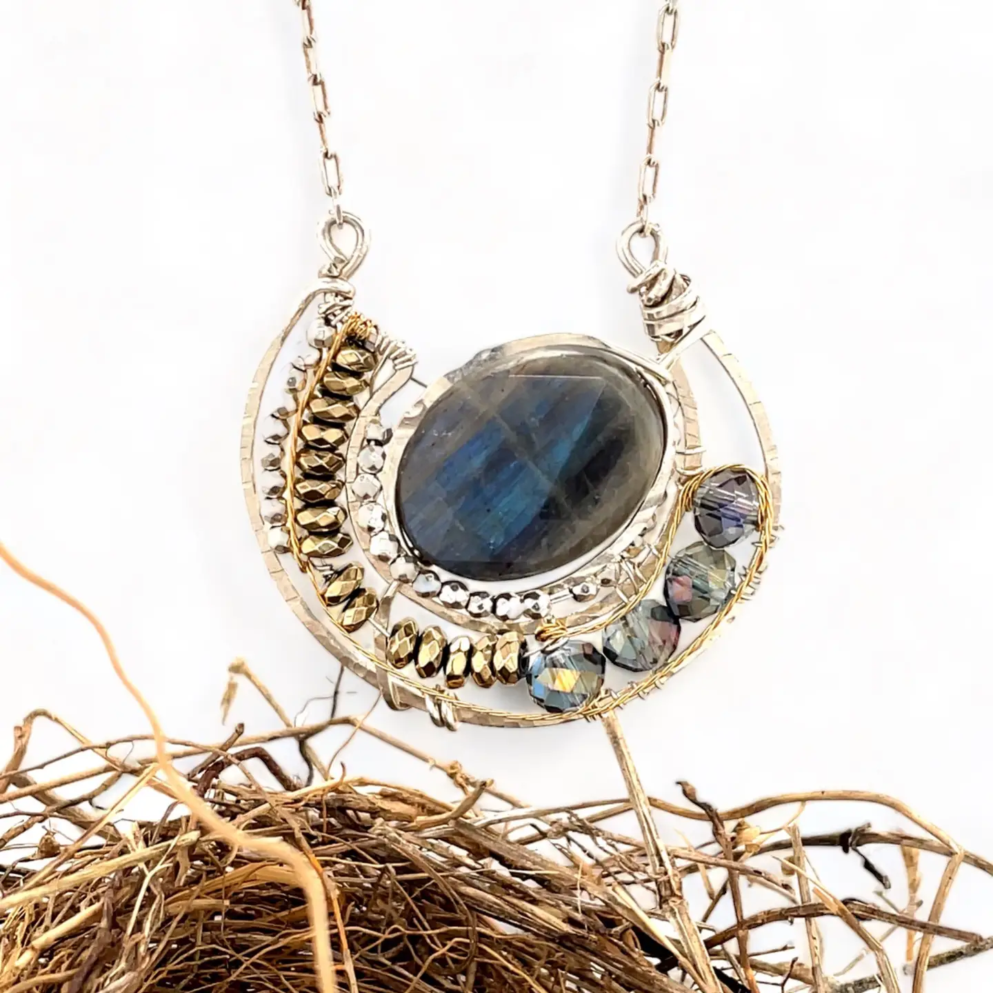 Faceted labradorite oval gemstones within a sterling silver pendant filled with pyrite gemstones and blue purple crystals and brass twist wire