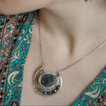 Faceted labradorite oval gemstones within a sterling silver pendant filled with pyrite gemstones and blue purple crystals and brass twist wire