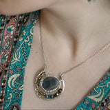 Faceted labradorite oval gemstones within a sterling silver pendant filled with pyrite gemstones and blue purple crystals and brass twist wire